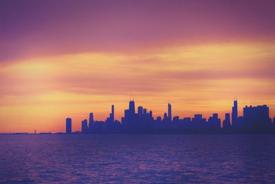 Sea with buildings in background at sunset