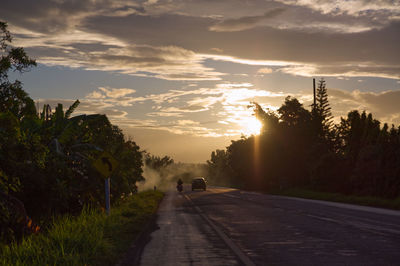 Road amidst trees against sky during sunset