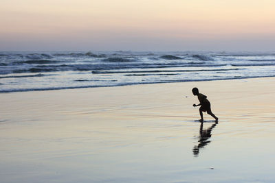 Full length of man on beach against sky during sunset