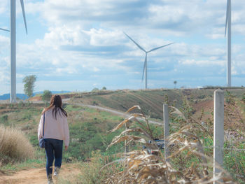 Asian woman walking and see on country road with sky ,cloudy and wind turbine background