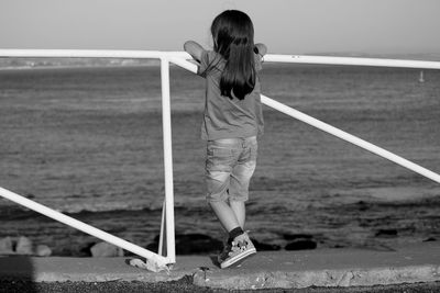 Rear view full length of girl standing by railing against sea