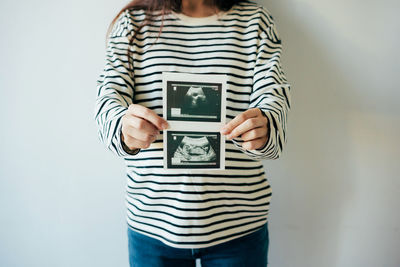 A woman in anticipation of the birth of a child holds an ultrasound scan in front of her.