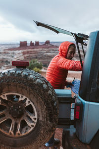 Woman in orange puffy reaches in to the back of her jeep at camp