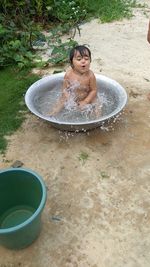 High angle view of cute baby girl sitting in container with water outdoors