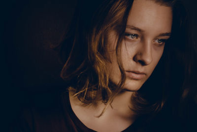 Close-up portrait of young woman against black background