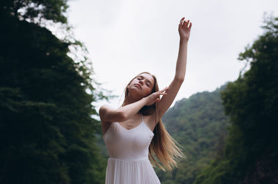 Full length of a smiling young woman standing against trees