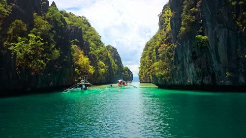 Boats sailing on sea amidst rocks against sky