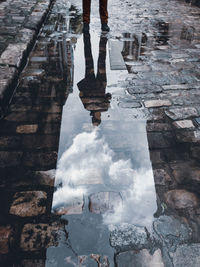 Low section of person standing on puddle in city during rainy season