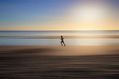 Silhouette person on beach against sky during sunrise