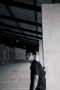 Young man looking away while standing against wall
