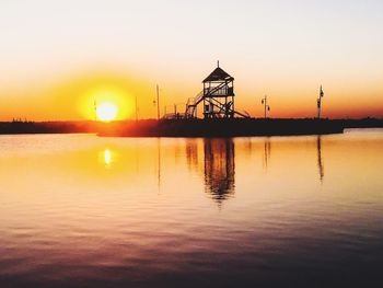 Silhouette cranes by sea against sky during sunset