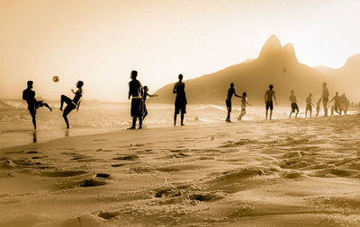 People playing soccer at beach against clear sky