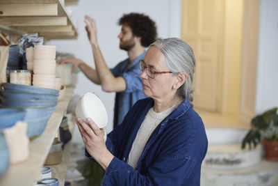 Man and woman arranging earthenware on shelf in art class