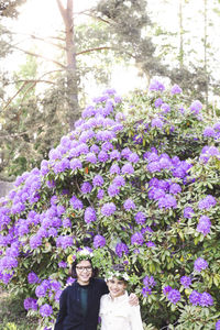 Portrait of happy brothers wearing tiaras standing against flowering plant at back yard