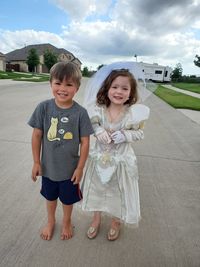 Portrait of kids playing bride and groom standing against sky