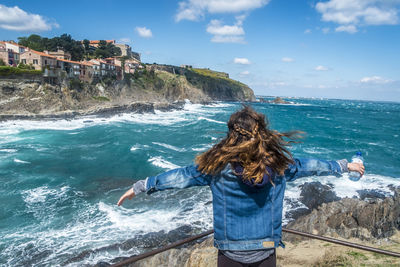 Rear view of woman standing with arms outstretched against sea