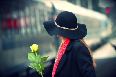 Side view of woman holding flower while standing at railroad station platform