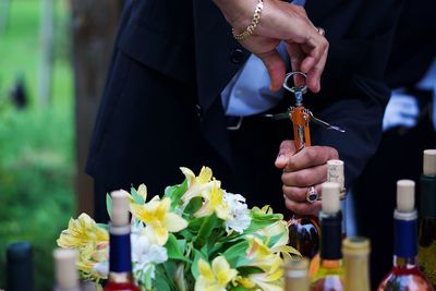 Midsection of groom opening wine during wedding