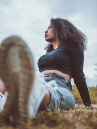 Side view of woman sitting on field against sky