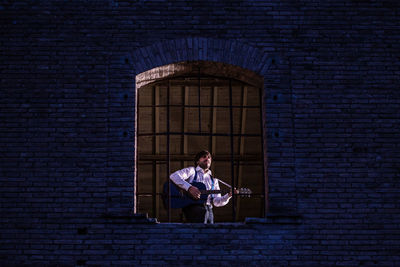 Low angle view of man playing guitar while standing at window