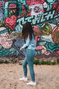 Young woman standing against graffiti wall at beach
