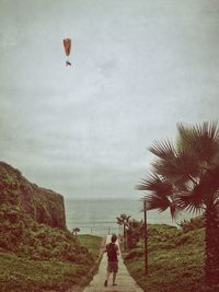 Rear view of man flying over beach against sky