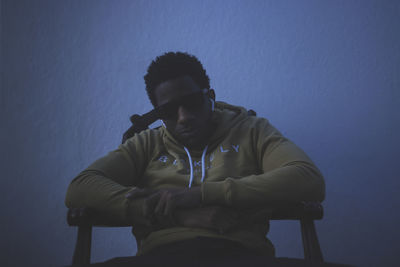 Man looking away while sitting on seat against blue wall