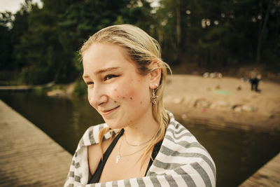 Smiling blond woman wearing towel at lake during vacation