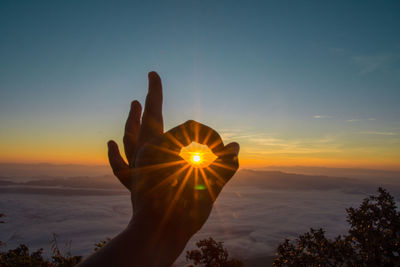 Optical illusion of cropped hand holding sun against blue sky during sunset