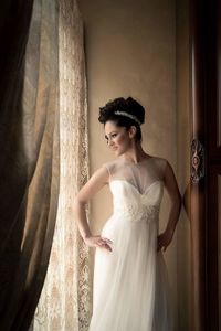 Bride with hands on hip standing by window