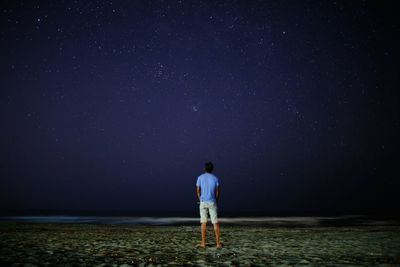 Full length rear view of man standing on beach at night