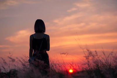 Rear view of woman standing on field against sky during sunset