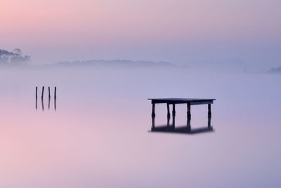 Silhouette wooden posts in lake against sky during sunset