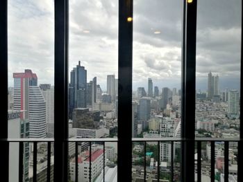 Buildings in city against sky seen through glass window