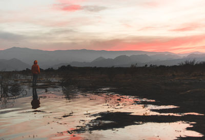 Man standing on shore against sky during sunset