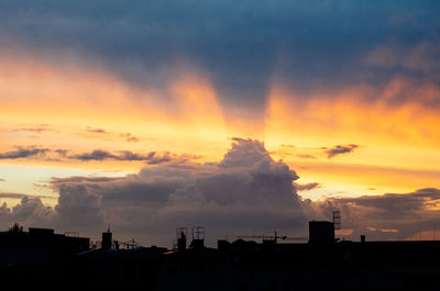 Silhouette cityscape against dramatic sky during sunset