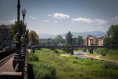 Bridge over river by buildings against sky