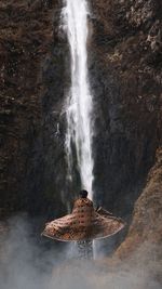 Rear view of woman standing against waterfall