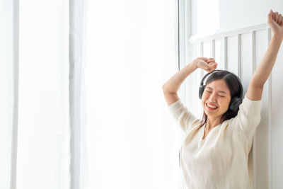 Happy young woman standing against wall