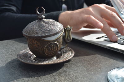 Close-up of coffee cup by person using laptop on table