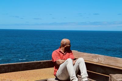 Man sitting on bench by sea against sky