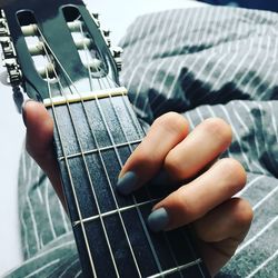 Cropped hand of woman playing guitar on bed