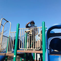 Low angle view of boy on playground against clear blue sky