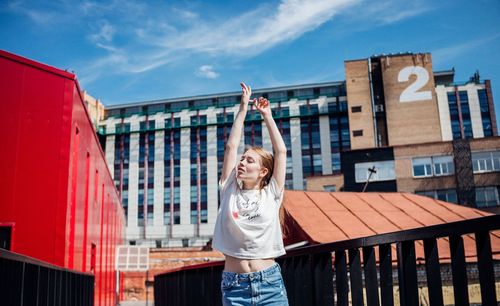 Young woman with arms raised standing against building