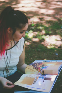 Woman looking at pictures on book while crouching at park