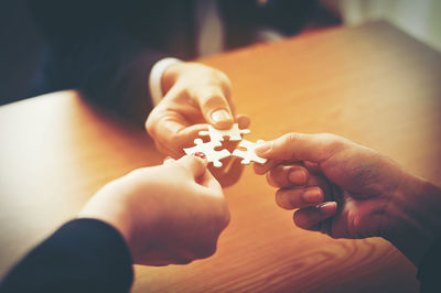 High angle view of people holding jigsaw piece on table