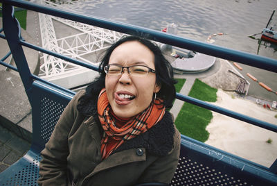 Portrait of smiling young woman sitting on bench by railing