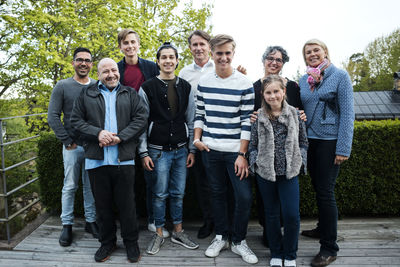 Portrait of happy multi-ethnic friends and family standing against hedge in yard