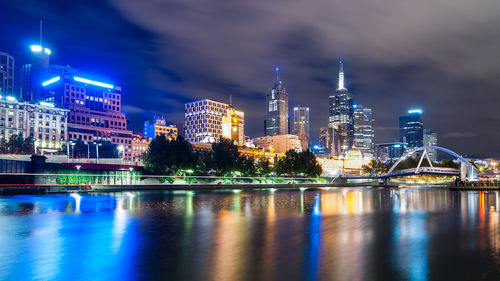 Illuminated buildings by river against sky at night