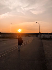 Rear view of man walking on road at sunset